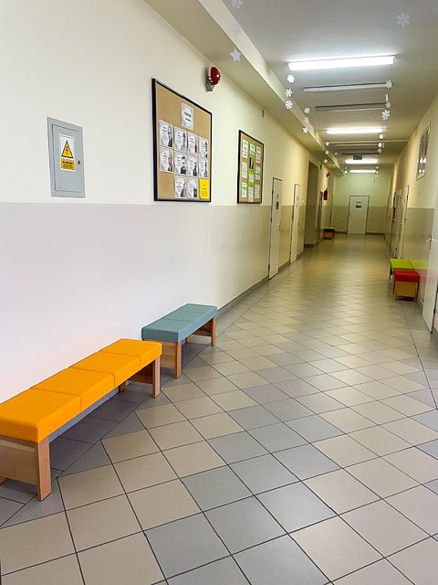 Ławka NORA II w buku naturalnym z żółtym siedziskiem na szkolnym korytarzu